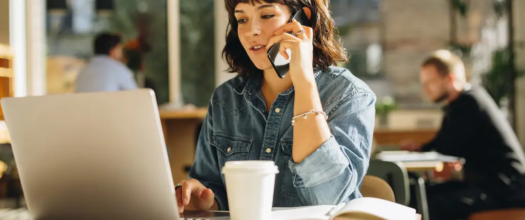vrouw telefoneert terwijl ze aan haar laptop werkt op café