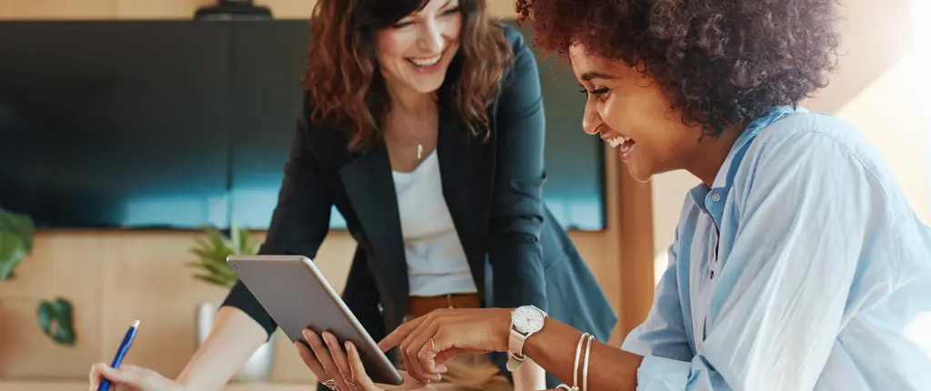 twee vrouwen lachen om iets dat op een tablet is weergegeven